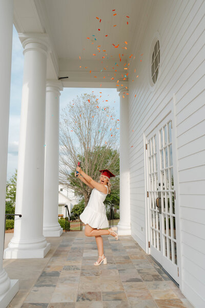 Young woman twirling under flying confetti on a white Southern-style porch during a joyful celebration session in Alabama — EC Photography