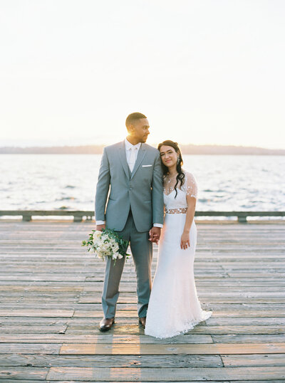 seattle wedding photographer captures wedding couple leaning on each other on lake dock at golden hour