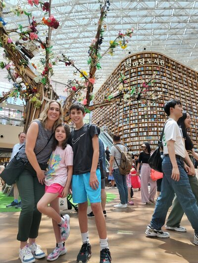 Meghan and her children in front of a floral display in an indoor market — Parenting Abroad category