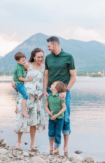 A happy family of 4 with 2 teen boys laughs while standing in a snowy mountain pass