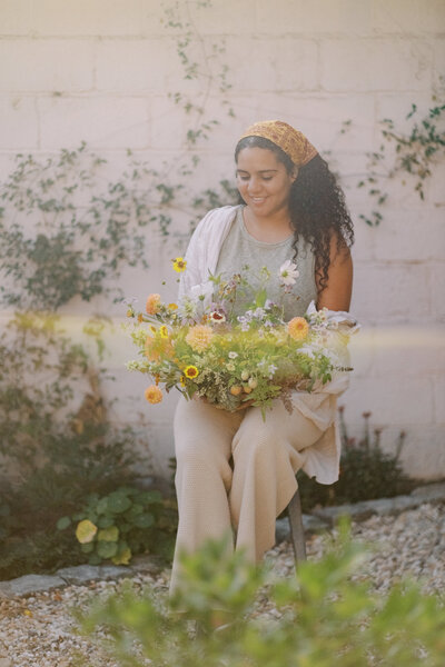 Natalia holds an arrangement, looking down at it and smiling.