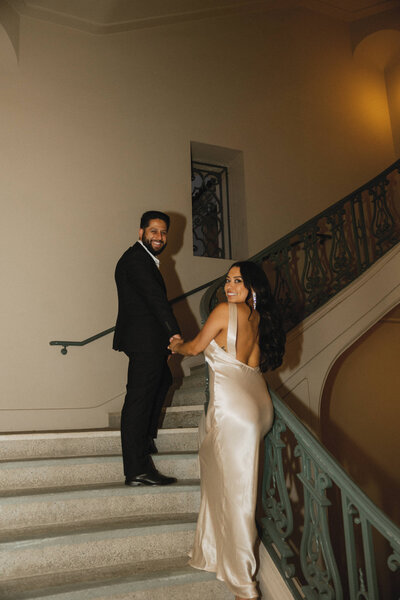 bride and groom standing on large stair case while holding hands