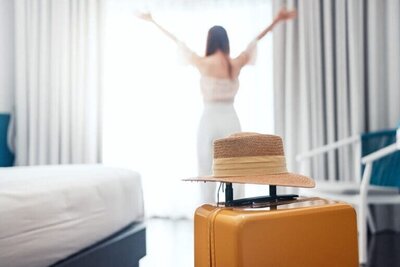 Female traveler arriving at upscale hotel suite with luggage and sunhat, ready for a personalized luxury vacation.
