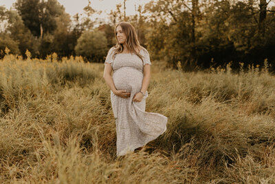 woman holding pregnant belly in field