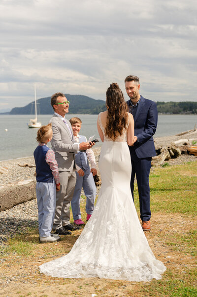 Bride and groom holding hands during a wedding ceremony with their family along the beach