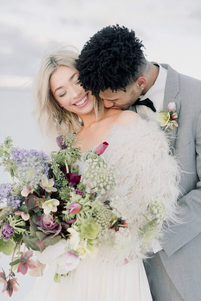 A groom kisses his bride's shoulder while at the Bonneville Salt Flats on their wedding day. 