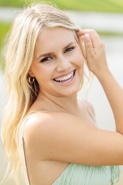 High school senior girl smiling at camera with her hand brushing away her hair. 