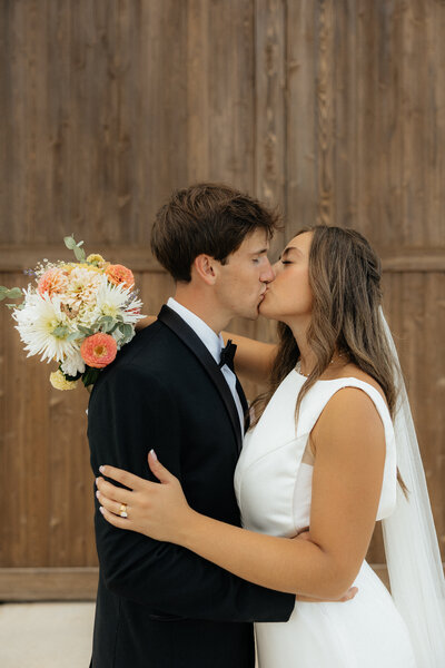 Olivia and Christian kissing in front of The Farmhouse Barn.