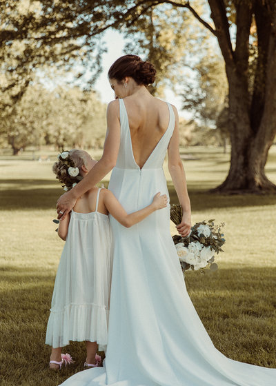 Flower girl and bride look at each other with their arms around one another's back
