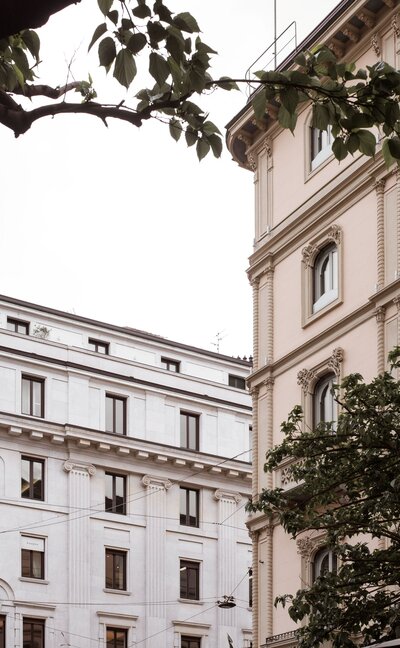 Two historic European Neoclassical buildings, one light beige with arched windows and fluted pilasters, and another white with grand fluted columns, showcasing classic architectural design and urban grandeur.