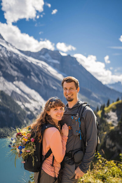 Man and woman hiker smile in front of snow capped mountains.