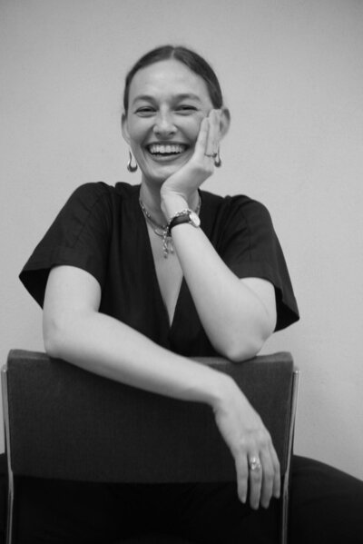 Close-up of Cora Demary laughing with her hand resting on her chin, looking off-camera.