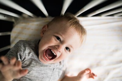 Happy toddler lying on a striped surface, smiling and looking upwards in a Pittsburgh lifestyle photography session.