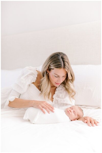 A mother lays on her bed and gazes down at her baby while being photographed by New Jersey Newborn Photographer Kate Voda