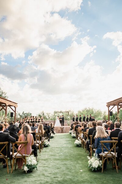 Wedding at Four Seasons at Troon North ceremony area with bride and groom standing at the alter and big beautiful clouds behind them