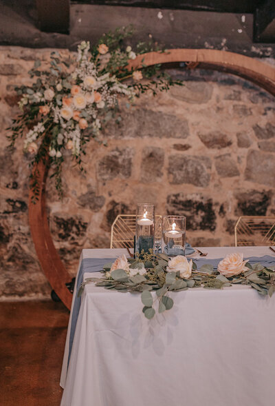 Sweetheart table with candles and floral décor against stone wall