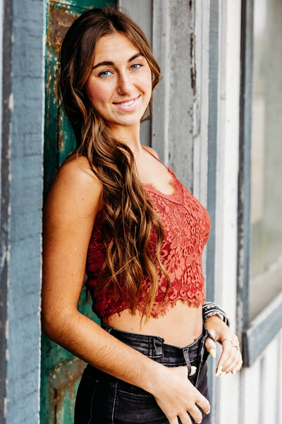 beautiful teenage girl with long brown hair in a orange top leaning against a blue and teal doorway near Green Bay WI