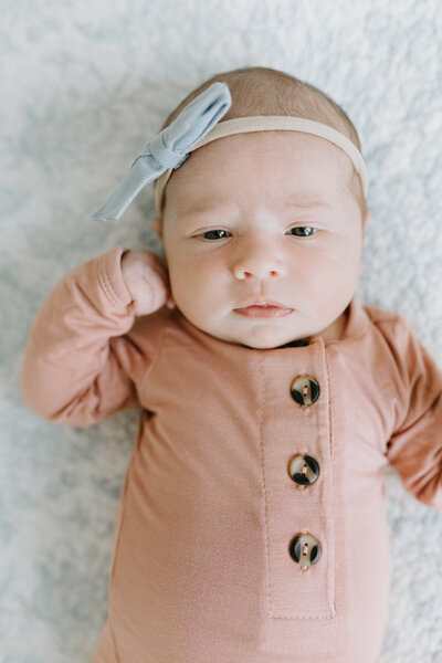 The newborn photo by Vanessa Stoller Photography of a baby girl with a blue bow laying on a blue quilt in Lafayette, Indiana. 