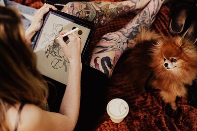 Kvinnlig tatuerare sitter och ritar upp design av tatuering på iPad.
