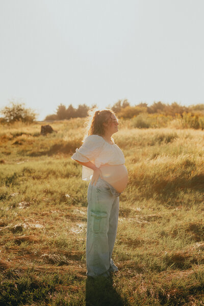 Photo of a pregnant woman standing face to the side with her hands on her back so you can see her baby bump taken by a langley photographer