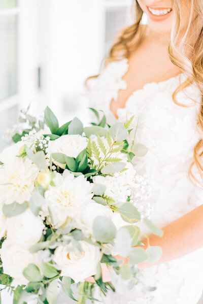 bride holding a beautiful light colored bouquet of flowers with roses and eucalyptus