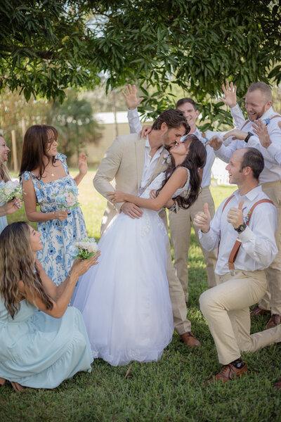 This image showcases a bride and groom doing a dip kiss while the bridal party celebrates them. 