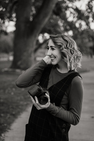 girl holds camera smiling on concrete path
