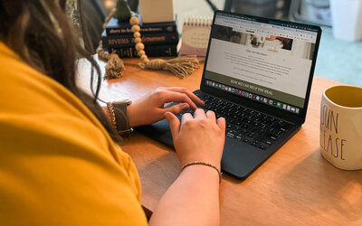 Close-up of hands typing on laptop showing a wellness website and surrounded by desk decor