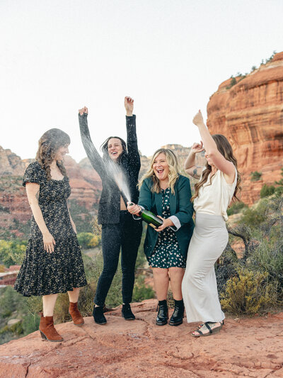 Four women toast to their journey with a burst of champagne, framed by the breathtaking red rock backdrop of Sedona—joyful, bold, and beautifully untamed.