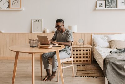 Man sitting in a chair at a table working from home at a laptop