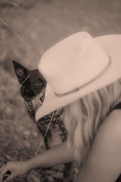 A  girl in a cowboy hat picks blackberries with a farm dog for her self love portraits.