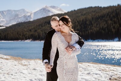 Colorado winter elopement photographer captures a bride and groom embracing by a snowy mountain lake in the Rocky Mountains.