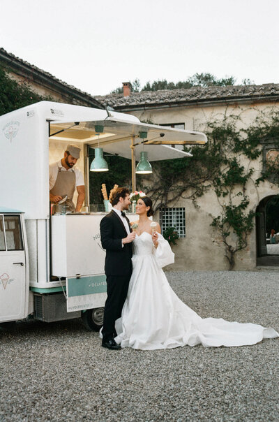 Bride and groom enjoying gelato from vintage cart at Villa Catignano in Tuscany during romantic courtyard wedding in Italy