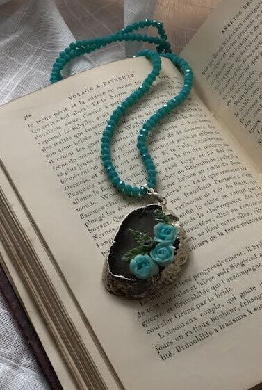 Open book with teal beaded necklace lying on top with brown pendant and teal flowers