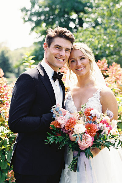 Joyful summer wedding portrait  at Gervasi Vineyard of bride and groom holding a vibrant bouquet of pink and coral flowers, photographed by Cleveland Ohio wedding photographer.