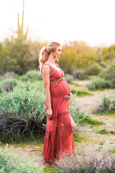 pregnant woman standing in the desert holding baby bump