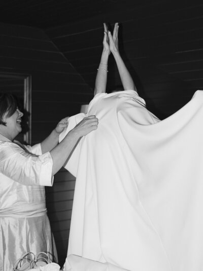 Black and white image of mom helping bride pull her dress down over her head