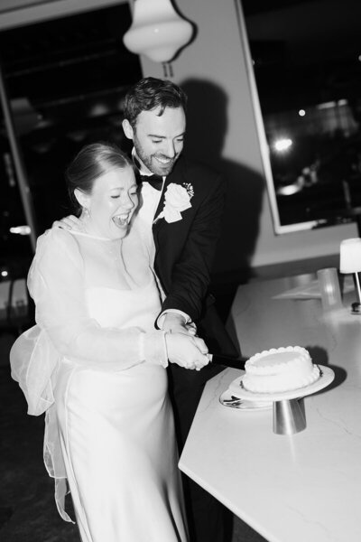 photo taken by tom thornton photography of bride and groom on their wedding day cutting cake in black and white image in minnesota