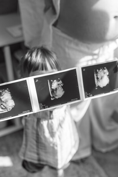 A toddler holding ultrasound pictures of sibling. 