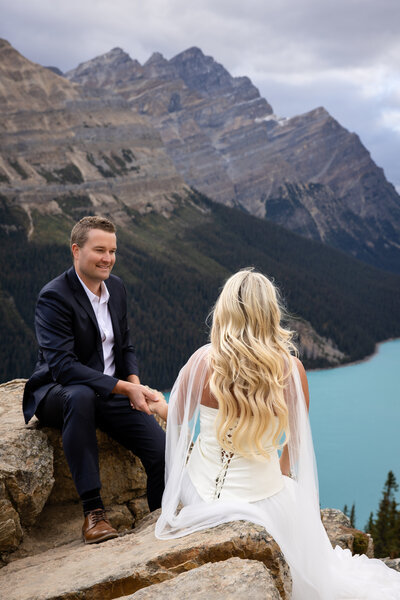 A couple in wedding attire sitting along the rock cliffs overlooking Peyto Lake 