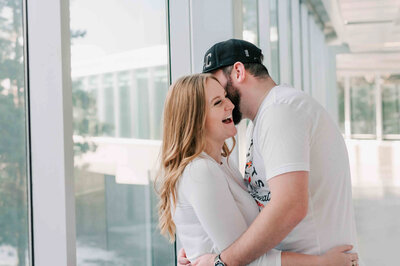 Husband stands behind wife with his arms around her.