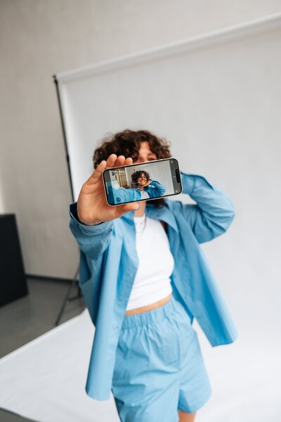 Vrouw in blauwe outfit maakt selfie tijdens branding shoot voor Studio Vers, gericht op webdesign en persoonlijke branding