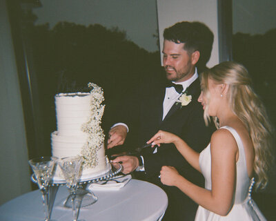 A man and woman joyfully cutting a wedding cake at a wedding in Columbus, Ohio shot with film photography. 