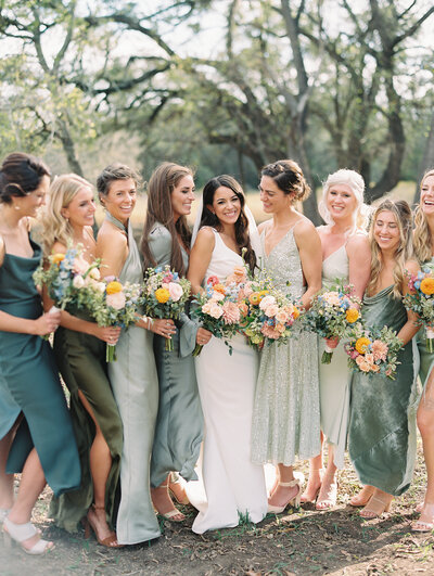 Bride with her bridesmaids in green dresses holding colorful bouquets