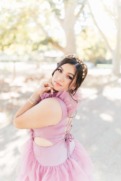girl with dark hair wearing whimsical puffy purple dress and gold head band posing for senior picture