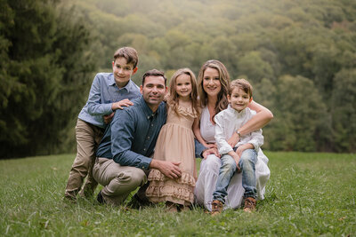 Family of five with arms around each other posing in green scenery