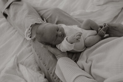 Newborn baby sleeping in mother’s lap during an intimate in-home family photoshoot in Maine, captured by fine art Photographer, Damini Photography.