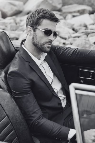 A handsome man in a tailored suit, driving a convertible with the rooftop down, exuding confidence in his decision.