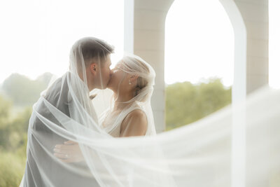 A couple kissing behind an intricate lace veil.
