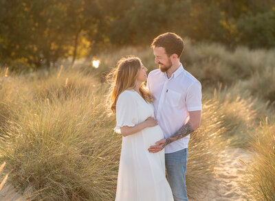Couple holding baby bump at sunset during outdoor maternity session in Poole, Dorset